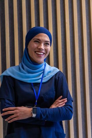 Smiling professional woman wearing hijab crossing arms at conference lanyard smartwatch