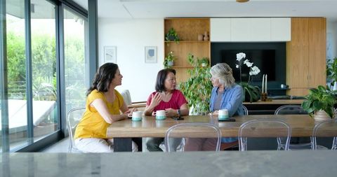 Three women enjoying coffee conversation at modern home dining table