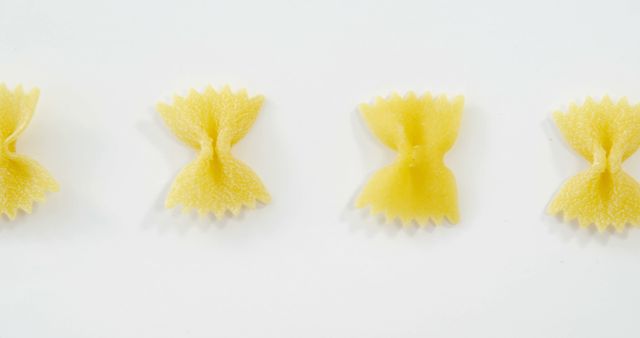 Bowtie pasta pieces are neatly lined up on a white background, illustrating simplicity and precision. Ideal for use in food blogs, Italian cuisine promotions, healthy eating campaigns, and culinary arts presentations.