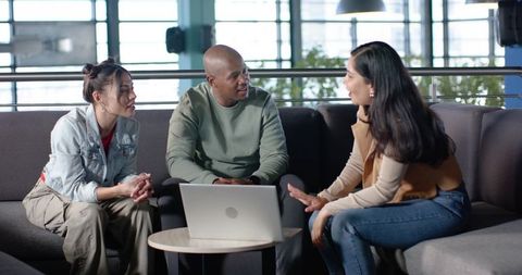 Collaborating coworkers discussing project in modern office lounge with laptop