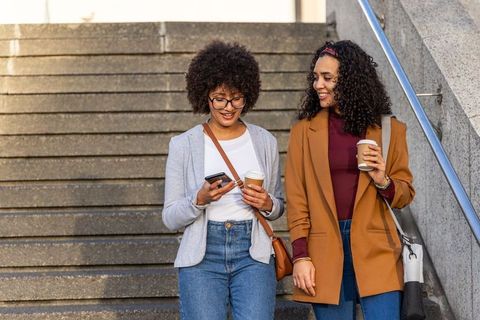 African american friends walking down urban steps holding coffee cups and checking phone