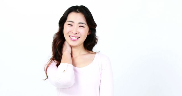 A young Asian woman smiles brightly, posing against a white background with copy space. Her cheerful expression and casual attire suggest a relaxed and happy mood.