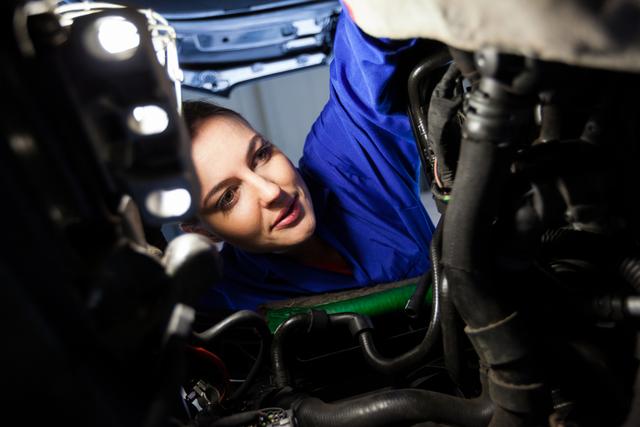 Close-up of female mechanic examining car engine within a repair garage. Ideal for illustrating skilled trades, gender diversity in workforce, auto repair shops, and technical skill training programs.