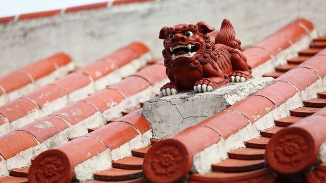 Perching red guardian lion on curved ceramic roof tiles with weathered cracked base detail