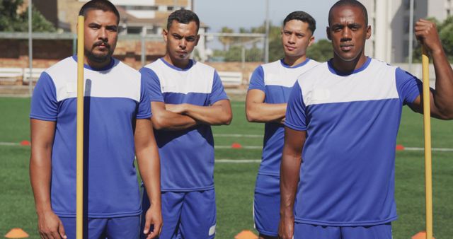 Portrait of diverse male football players wearing blue uniforms training on outdoor pitch. Football, sports, fitness and teamwork.