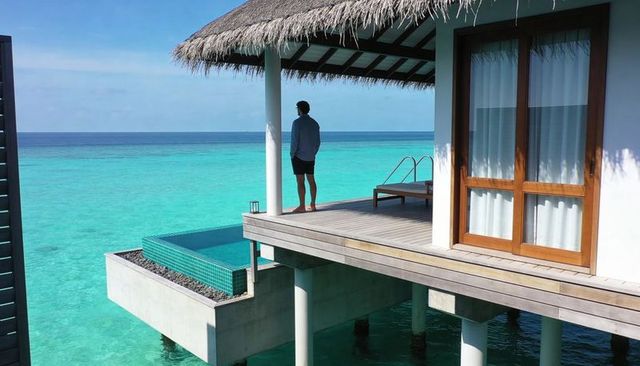Man standing on overwater villa deck overlooking turquoise ocean with plunge pool