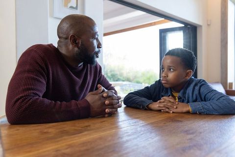 African american father and son having heartfelt conversation at wooden dining table, natural light