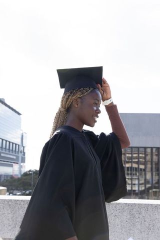 African american graduate wearing mortarboard and gown on urban rooftop celebrating achievement