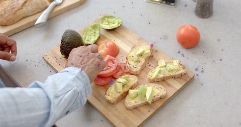 Preparing avocado toast with fresh tomato slices on rustic bread cutting board
