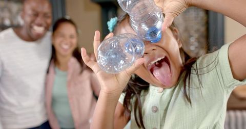 Playful Child Using Water Bottles as Glasses with Parents in Background