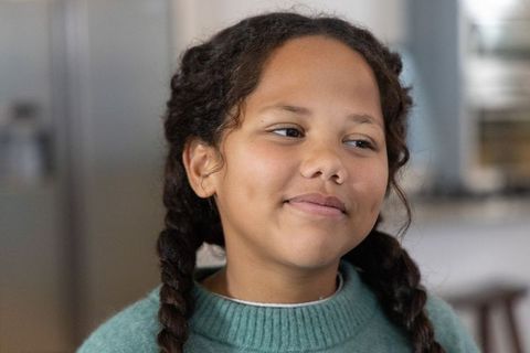 Smiling school-age girl wearing teal sweater looking right in cozy kitchen portrait