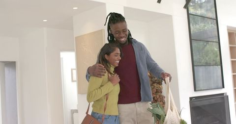 African american man and indian woman embracing while entering sunlit modern home