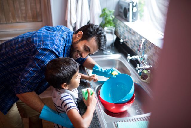 Father and son washing dishes together in kitchen, promoting family bonding and teamwork. Ideal for use in parenting blogs, family-oriented advertisements, and articles about household chores and domestic life.
