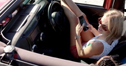 Young Woman Relaxing in Car Using Smartphone During Road Trip