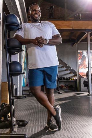 Confident african male leaning on medicine-ball rack smiling after gym strength training