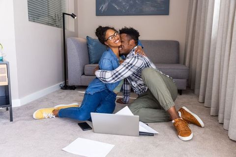 Young couple embracing on living room floor using laptop and papers for remote work