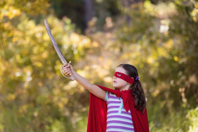 Little girl holding sword while wearing superhero costume in forest