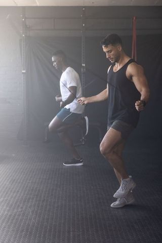 Two men skipping rope in gym performing high-intensity cardio and strength training