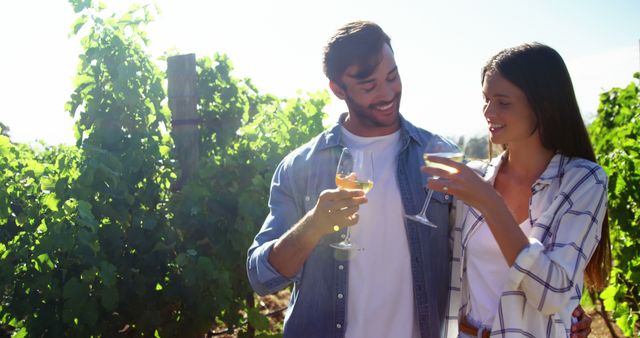 A young Caucasian couple enjoys a wine tasting experience in a vineyard, with copy space. Their casual attire and cheerful interaction suggest a relaxed and romantic outing.