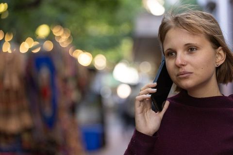 Young woman talking on phone at twilight market with bokeh string lights and textiles