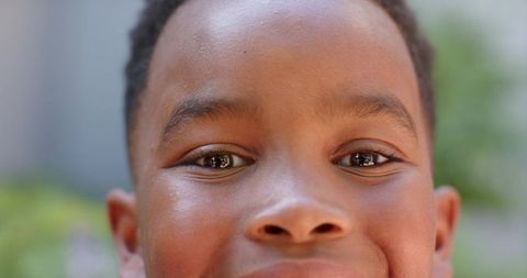 Smiling school-age boy close-up looking at camera with eye reflections and soft bokeh