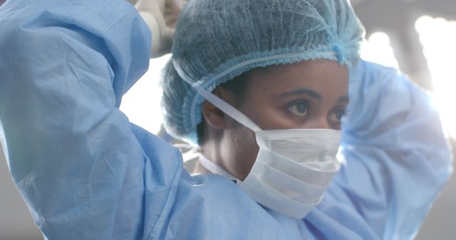 African american female surgeon wearing face mask in operating theatre. Medicine, healthcare, surgery, hospital and work, unaltered.