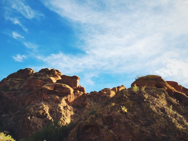 Photograph of a rugged rocky formation set against a blue sky with a few clouds. Ideal for use in travel blogs, desert tourism advertisements, nature documentaries, geological studies, and wallpapers highlighting natural landscapes.