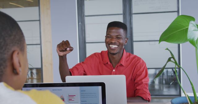Happy african american creative businessman fistbumping with female colleague at desk in office. business and technology in office workplace.