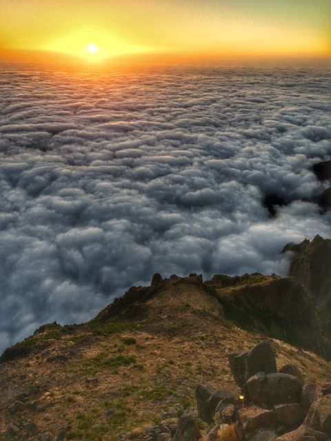 Sun setting over a blanket of clouds as seen from a mountain peak. Ideal for travel brochures, nature photography portfolios, inspirational backgrounds, or desktop wallpapers. It captures the serene and breathtaking beauty of mountain ranges at twilight.