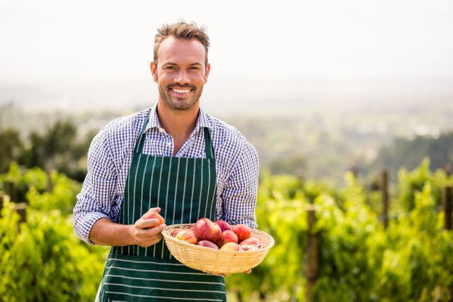 Portrait of smiling young man holding apple basket at vineyard