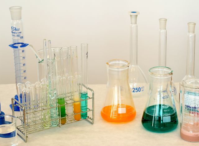 Laboratory glassware filled with colorful chemical solutions, including beakers, test tubes, measuring cylinders, and flasks. Ideal for illustrating scientific research, chemistry education, laboratory experiments, and professional scientific settings.