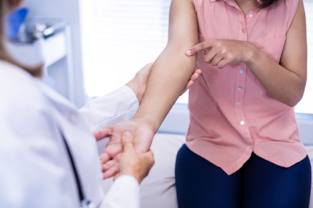 Female patient sitting in a medical clinic. Doctor examining her arm during a consultation. Ideal for healthcare, medical, diagnostic, and treatment-related content. Suitable for articles, blogs, and educational material on medical checkups, patient care, and doctor-patient interactions.