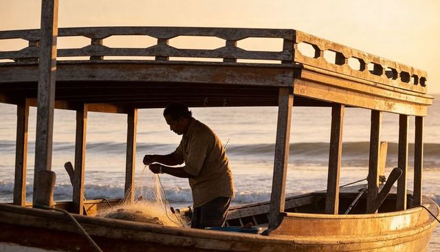 Solitary indian fisherman mending net on wooden boat at sunrise golden hour seascape