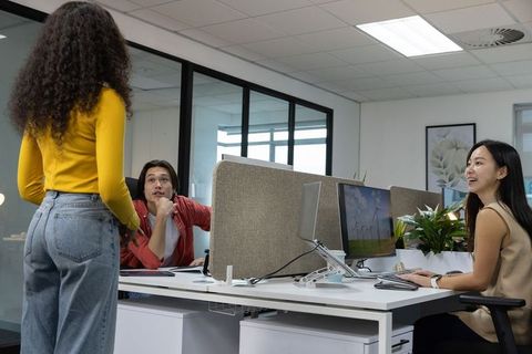 Team collaborating in open-plan office while woman in yellow top presenting idea
