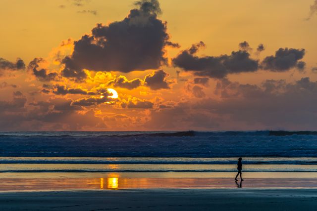 Individual Walking Along Beach at Sunset Under Vibrant Sky - Download Free Stock Photos Pikwizard.com