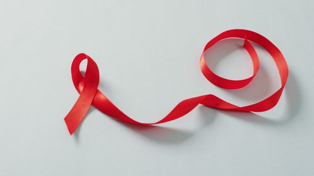 Red ribbon symbol on a grey background used for promoting cancer awareness and health prevention campaigns. Ideal for use in medical presentations, educational materials, and health awareness promotions.