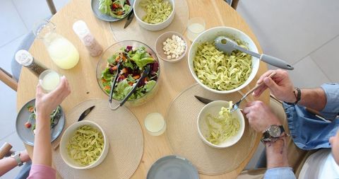 Couple sharing pesto fettuccine with fresh salad and lemonade on wooden table