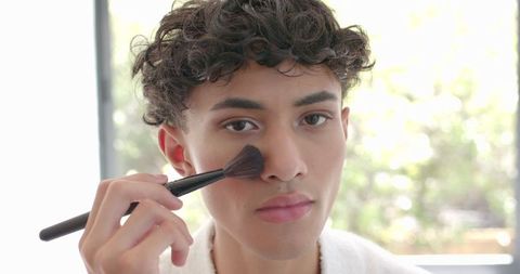 Man Applying Makeup Brush in Daylit Room for Skincare Routine