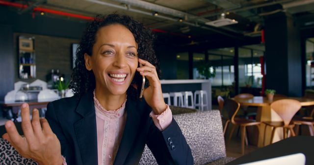 African-American businesswoman smiling and talking on phone in modern office setting. Ideal for business communication, work environment, professional success, and corporate lifestyle themes. Can be used in presentations, marketing materials, and websites showcasing professional services, business success stories, or modern office spaces.