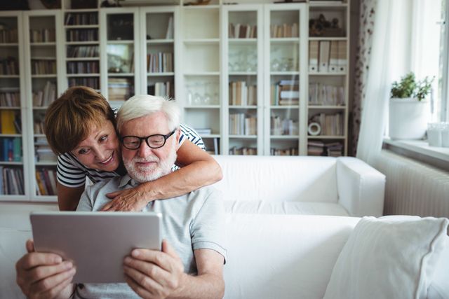 Senior couple bonding over a digital tablet in a bright and cozy living room. Perfect for illustrations of retirement lifestyle, elderly people embracing technology, and family togetherness in a home setting.
