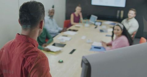 Man presenting to team in modern conference room with laptop, projector and documents