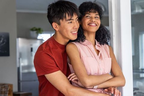Mixed-race couple embracing in sunlit kitchen, smiling, cozy home romance and togetherness