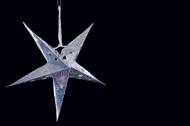 This image features a close-up view of a parol, a traditional Filipino Christmas lantern, hanging against a black background. The shiny, metallic star-shaped decoration is commonly used during the holiday season. Ideal for use in holiday-themed promotions, cultural celebrations, festive event invitations, and Christmas decor inspiration.