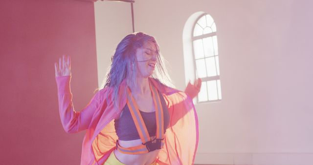 Woman with long hair dancing passionately with colorful lighting in an indoor space. She is wearing bright clothes and appears energetic and free-spirited. Great for articles or advertisements about creativity, self-expression, dance performances, fitness routines, or artistic events.