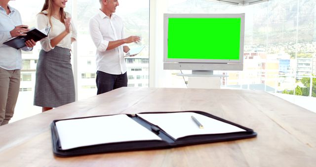Business team engaged in a presentation in a modern office with a blank green screen monitor in the background, suggesting a versatile template for corporate, advertising, or marketing purposes. Ideal for presentations, demonstrating teamwork and professional environments. The photo can be used for business, workplace productivity, and meeting-related content.