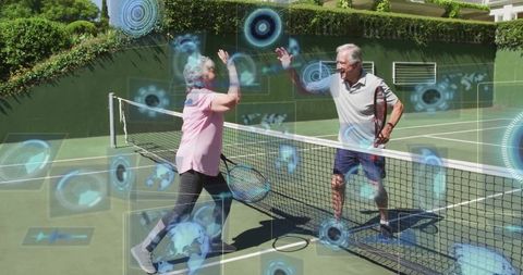 Energetic Senior Couple High-Fiving on Outdoor Tennis Court with Futuristic Technology
