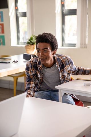 African American student leaning and reaching for pen by laptop in bright study lounge