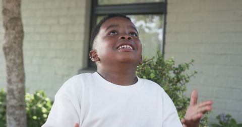 Joyful child looking up on sunlit porch wearing white shirt, playful outdoor moment
