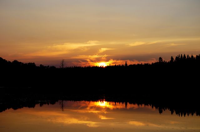 Stunning sunset over a forested lake with vibrant, colorful sky reflecting on the calm water. Ideal for backgrounds, nature-themed projects, conservation articles, and travel brochures.