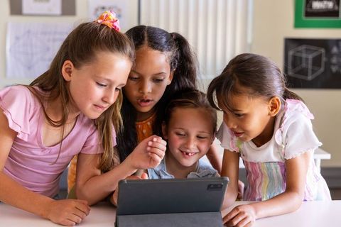 Multicultural girls collaborating around tablet in classroom learning geometry and coding